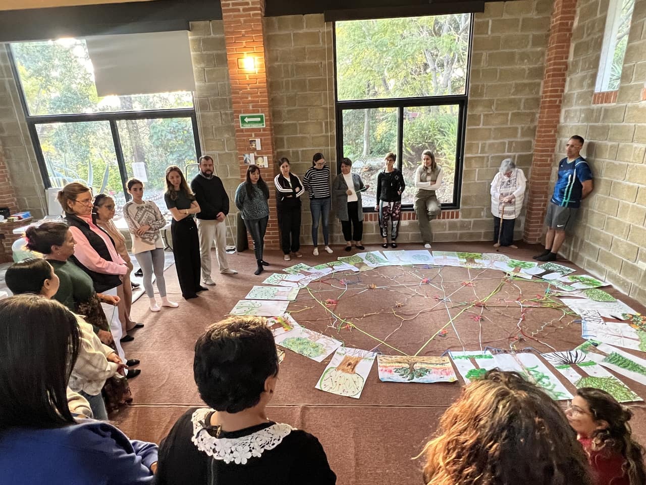 Participantes del retiro de pie en círculo alrededor de un mandala en el salón
